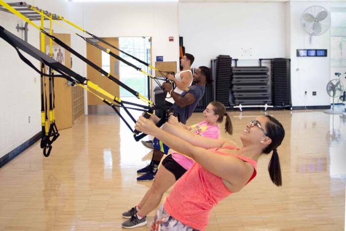 学生们在活动室的集体健身课上使用TRX腕带进行锻炼.